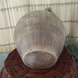 May include: A large, round, brown ceramic vase with a textured surface. The vase is sitting on a woven wicker base.