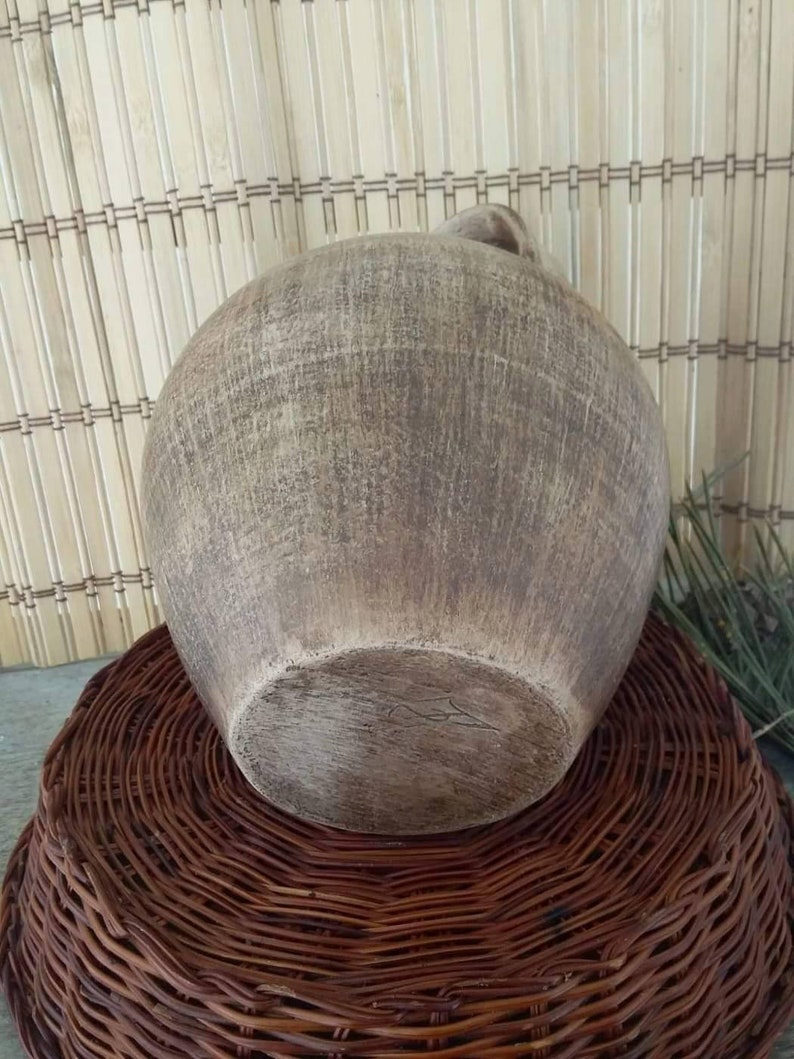 May include: A large, round, brown ceramic vase with a textured surface. The vase is sitting on a woven wicker base.