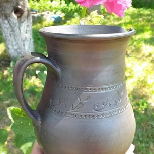 May include: A dark gray ceramic pitcher with a handle and intricate floral designs carved into the surface.