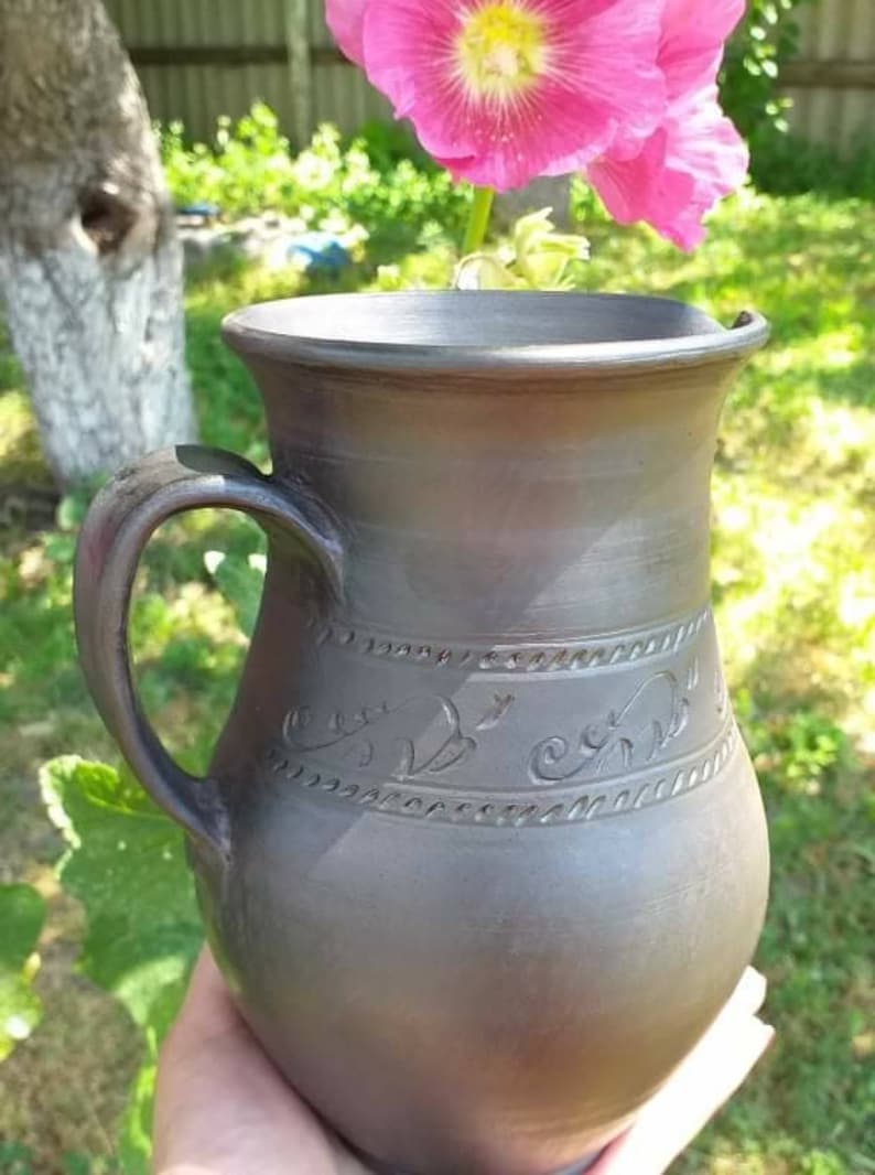 May include: A dark gray ceramic pitcher with a handle and intricate floral designs carved into the surface.