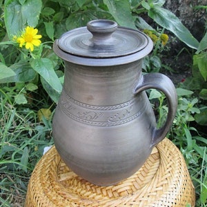 May include: A dark brown ceramic pitcher with a lid and a handle. The pitcher has a decorative design around the middle.