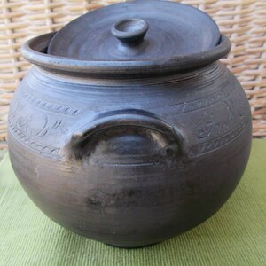 May include: A black ceramic pot with a lid and a handle. The pot has decorative carvings around the sides.