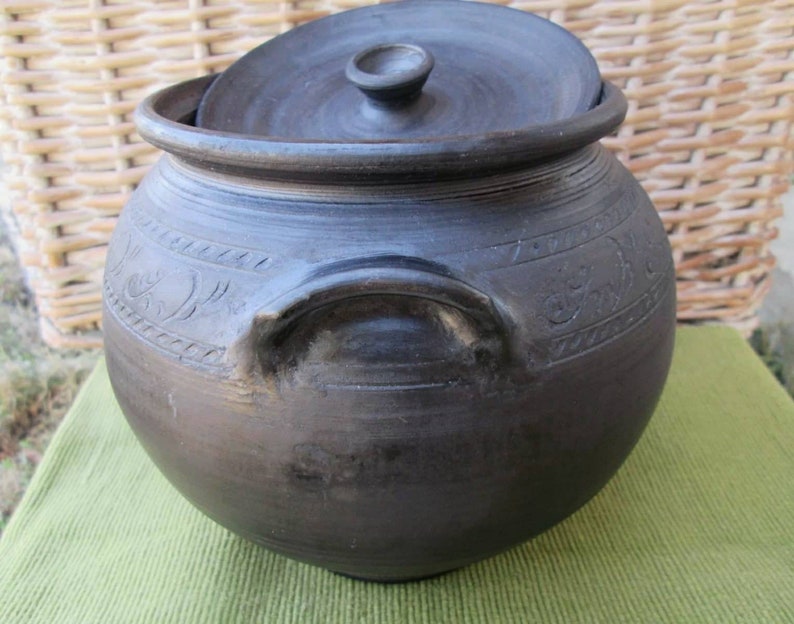 May include: A black ceramic pot with a lid and a handle. The pot has decorative carvings around the sides.