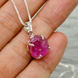 Puede incluir: Un collar de cadena de plata con un colgante de piedra preciosa rosa. La piedra preciosa es un rubí natural en bruto con un corte facetado.