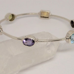 Op de afbeelding: Een zilveren armband met zes edelstenen: amethyst, citrine, aquamarijn, zwarte onyx en twee heldere stenen.