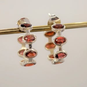May include: Silver hoop earrings with a row of five red gemstones.