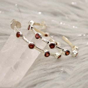 May include: Silver hoop earrings with red gemstone accents. The earrings are double-layered and have a polished finish.