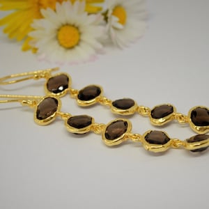 May include: A pair of long, gold-toned earrings with brown gemstone drops. Each earring has five oval-shaped gemstones connected by gold-toned links.