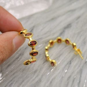 May include: Gold hoop earrings with red oval-shaped gemstones.