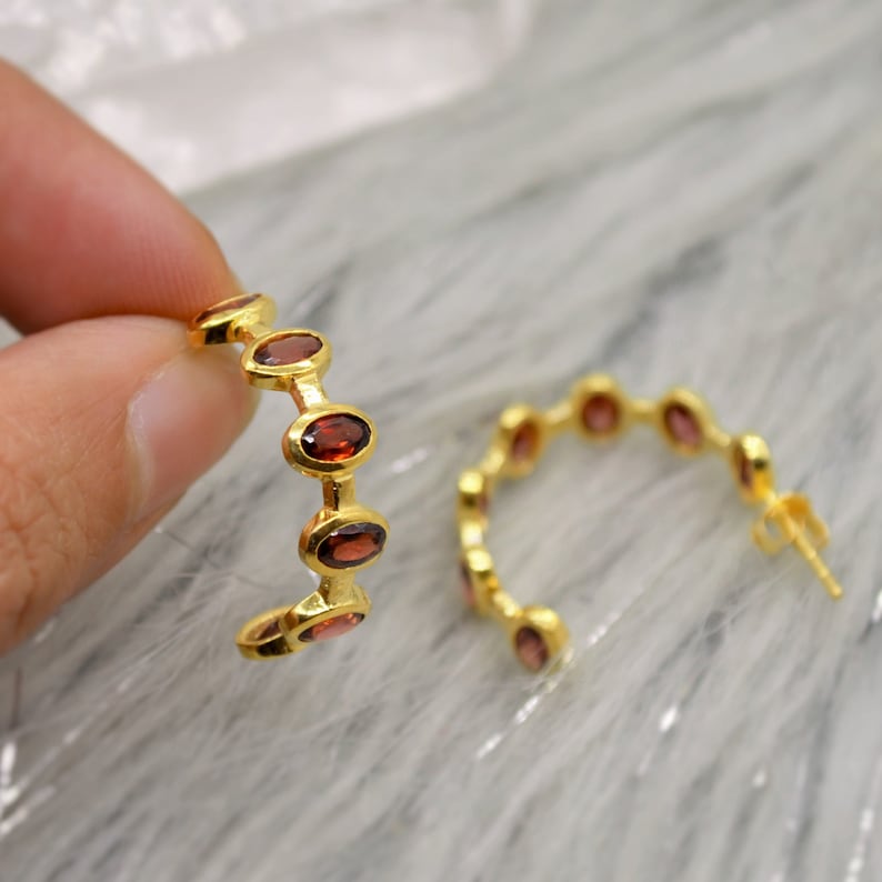 May include: Gold hoop earrings with red oval-shaped gemstones.