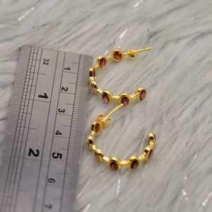 May include: Gold hoop earrings with small, round, pink gemstones. The earrings are approximately 1.5 inches in diameter.