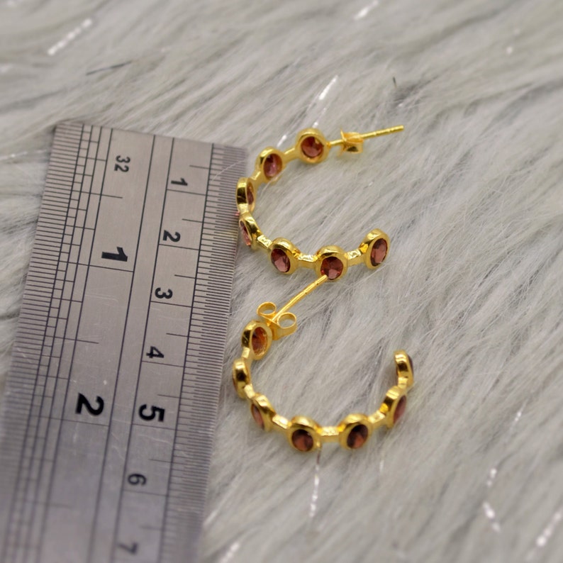 May include: Gold hoop earrings with small, round, pink gemstones. The earrings are approximately 1.5 inches in diameter.