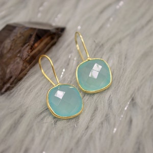 Peut inclure: Une paire de boucles d'oreilles en or avec des gouttes de pierres précieuses bleu clair. Les boucles d'oreilles ont une forme carrée et un design délicat.