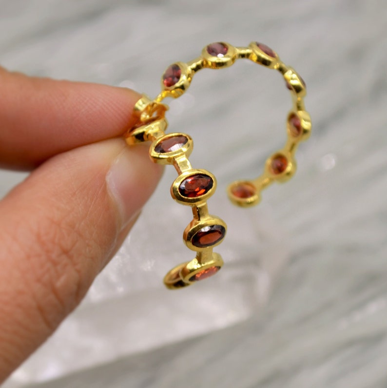 May include: Gold hoop earrings with a row of oval-shaped red gemstones.