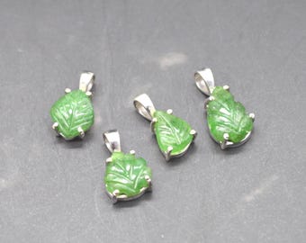 May include: Four green leaf-shaped pendants with silver-colored bails. The pendants are carved with leaf details and set in silver-colored metal. The pendants are displayed on a gray surface.