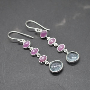 May include: Silver drop earrings with a sequence of oval pink gemstones and a teardrop-shaped, pale blue gemstone at the base. The earrings have a simple hook design.
