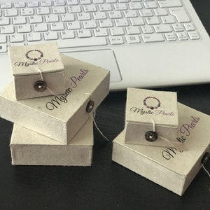 May include: Four small, rectangular boxes made of brown paper with the text "Mystic Pearls" printed on them. The boxes are stacked on top of each other.