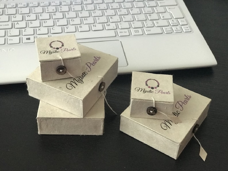 May include: Four small, rectangular boxes made of brown paper with the text "Mystic Pearls" printed on them. The boxes are stacked on top of each other.