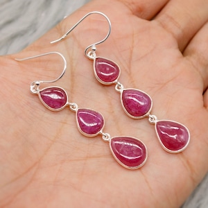 Peut inclure: Boucles d'oreilles pendantes en argent avec trois pierres précieuses rouges en forme de goutte d'eau. Les boucles d'oreilles ont un design simple avec une fermeture à crochet. Les pierres sont serties dans une lunette en argent.