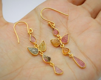 May include: A pair of gold dangle earrings with multiple teardrop-shaped gemstones in shades of pink, yellow, and green.