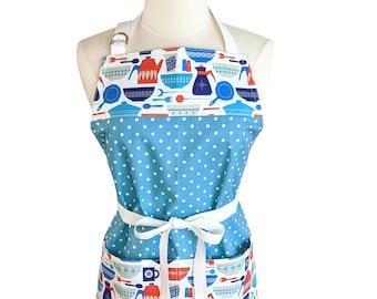 May include: A blue polka-dot apron with a white tie and pockets. The top and pockets feature a pattern of kitchen utensils in red, blue, and white. The apron is displayed on a mannequin.