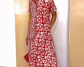 May include: A red and white patterned maxi dress with short sleeves and a collared neckline. The dress features a button-down front and a split design, with a different pattern on the left side. The person is wearing sunglasses and earrings.