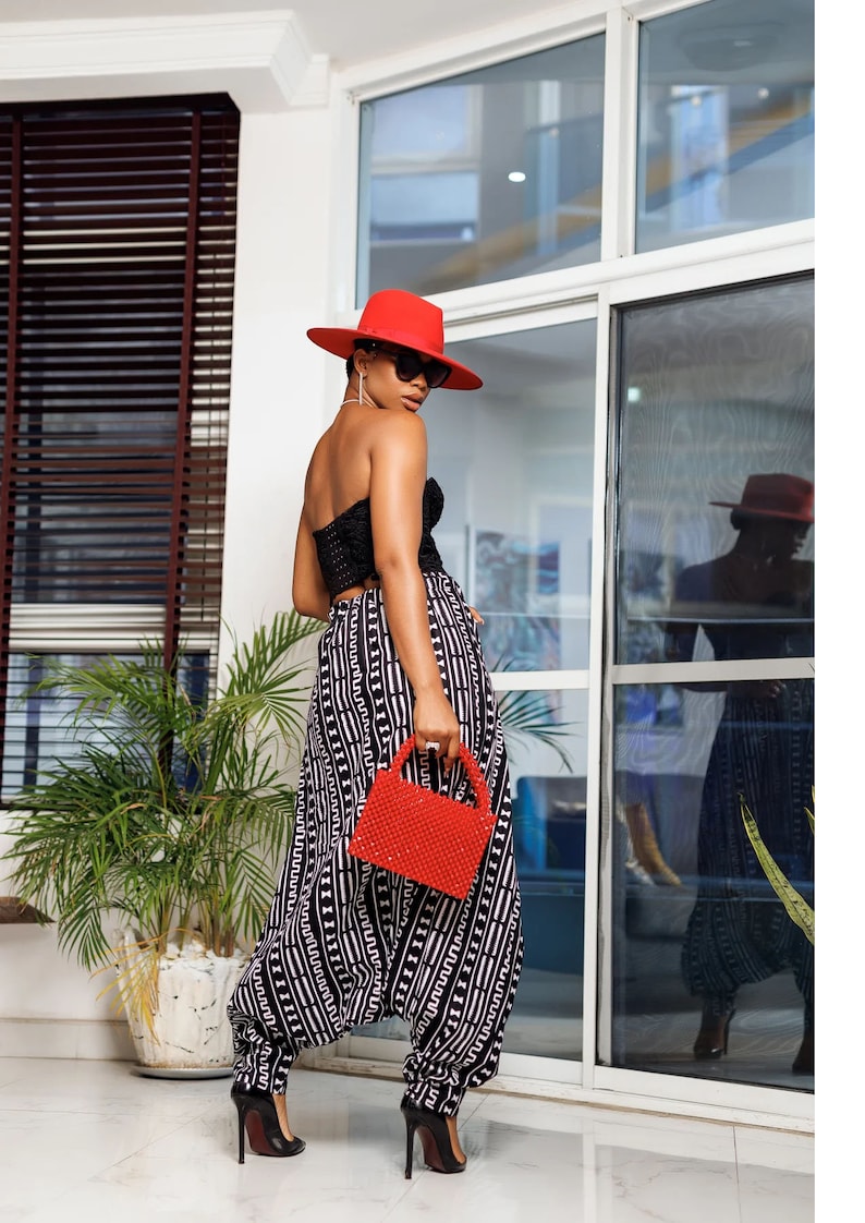 May include: A woman wearing a black and white patterned jumpsuit with a red hat and red beaded handbag.