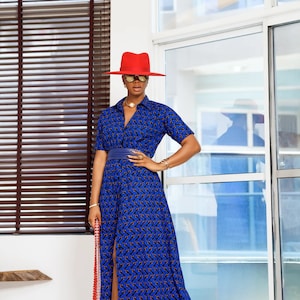 May include: A woman's blue maxi dress with a geometric pattern, short sleeves, and a high slit. The dress is paired with a red hat, gold sandals, and a beaded handbag. The outfit is accessorized with gold jewelry.