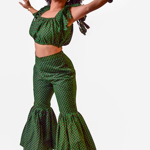 Puede incluir: Conjunto de top corto y pantalón acampanado verde con un patrón repetido de pequeñas formas rojo oscuro. El top tiene mangas con volantes y el pantalón tiene una pernera ancha y acampanada. El conjunto es de tejido ligero.