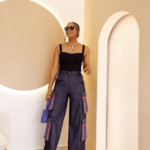 May include: A woman wearing a black tank top and dark blue wide-leg pants with decorative trim. She is holding a small blue beaded bag and wearing sunglasses.