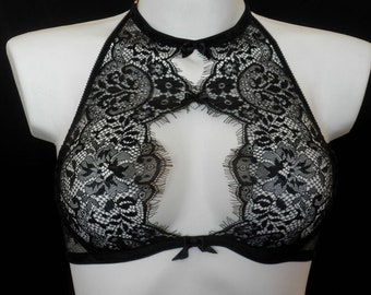 Pode incluir: Sutiã halter de renda preta com design de fechadura. O sutiã apresenta intrincados padrões de renda floral e pequenos detalhes de laço. O sutiã é exibido em um manequim branco contra um fundo preto.