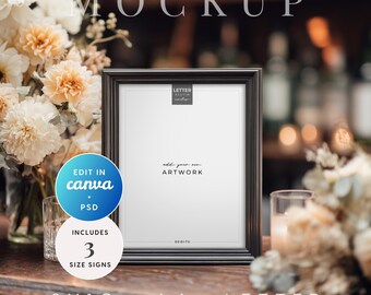 May include: A black framed mockup with the text "MOCKUP" at the top. The frame is on a wooden surface, with flowers on either side. The frame includes the text "add your own ARTWORK". The image also includes the text "EDIT IN canva + PSD" and "INCLUDES 3 SIZE SIGNS".