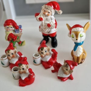 Może przedstawiać: Zbiór świątecznych figurek vintage, w tym Świętego Mikołaja, elfów i renifera. Figurki są wykonane z ceramiki i pomalowane żywymi kolorami.