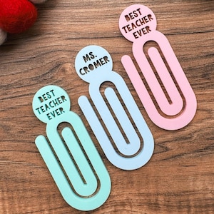 May include: Three colorful paperclip bookmarks with personalized messages. The bookmarks are light blue, pink, and green. The messages on the bookmarks read "Best Teacher Ever", "Ms. Cromer", and "Best Teacher Ever".