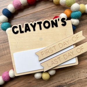 K&ouml;nnte beinhalten: Ein Holzschild mit dem Namen "CLAYTON'S" in schwarzen Buchstaben. Das Schild hat einen leeren Platz zum Schreiben und zwei Holzbanner, auf denen "ERSTER TAG VON" und "LETZTER TAG VON" steht.