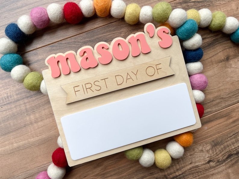 K&ouml;nnte beinhalten: Ein Holzschild mit dem Text "mason's first day of" in rosa Buchstaben. Das Schild hat einen leeren wei&szlig;en Bereich zum Schreiben des Datums.