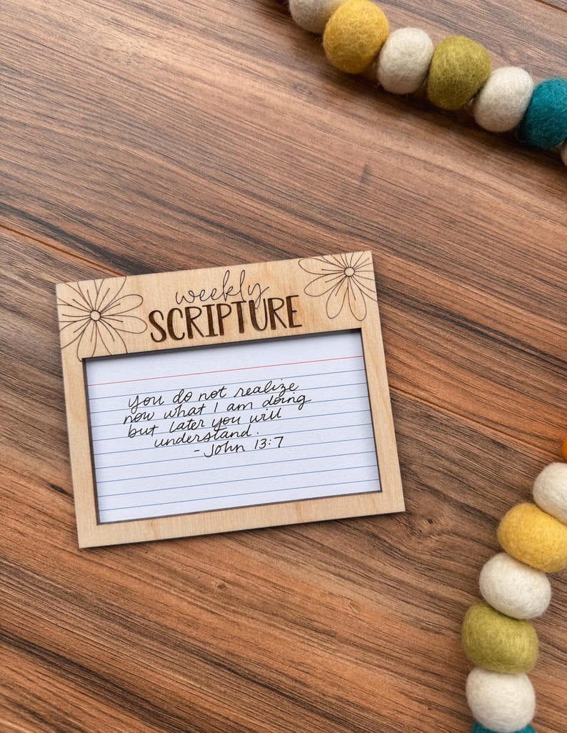 Może przedstawiać: Drewniana ramka na cotygodniowe Pismo Święte z odręczną notatką. Ramka ma kwiatowe akcenty i napis "weekly SCRIPTURE". Notatka brzmi: "You do not realize now what I am doing but later you will understand. - John 13:7".
