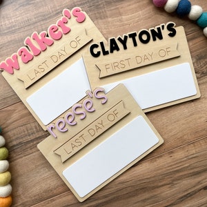 K&ouml;nnte beinhalten: Drei Holzschildchen mit leeren Feldern zum Beschreiben. Die Schilder sind mit rosa, lila und schwarzen Buchstaben verziert. Die Schilder zeigen "Walker's Last Day Of", "Clayton's First Day Of" und "Reese's Last Day Of".