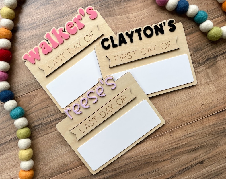 K&ouml;nnte beinhalten: Drei Holzschildchen mit leeren Feldern zum Beschreiben. Die Schilder sind mit rosa, lila und schwarzen Buchstaben verziert. Die Schilder zeigen "Walker's Last Day Of", "Clayton's First Day Of" und "Reese's Last Day Of".