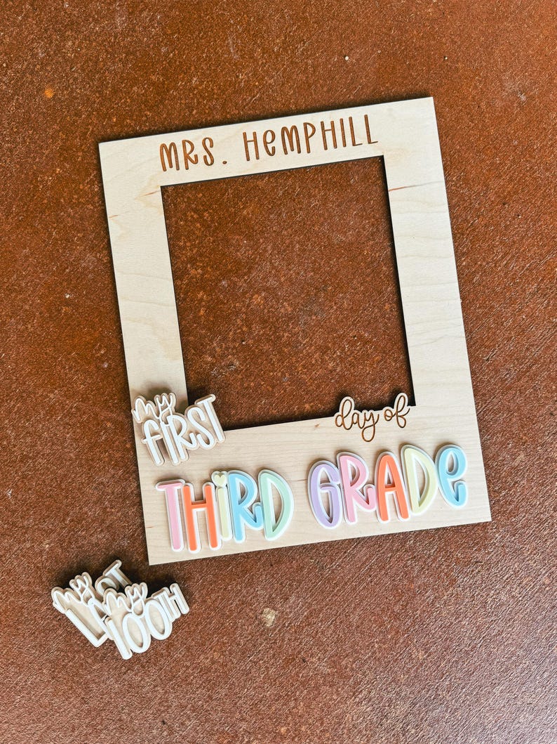 May include: A wooden photo frame with the text "MRS. HEMPHILL" at the top. Below, the words "MY FIRST" and "day of THIRD GRADE" are attached. A separate piece reads "100th day". The frame has a natural wood finish.
