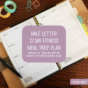 Puede incluir: Un planificador abierto a un plan de preparación de comidas, con el texto "HALF LETTER 21 DAY FITNESS MEAL PREP PLAN." El planificador está en una carpeta de cuero beige con pestañas coloridas. También se ven un bolígrafo, cinta adhesiva y clips.