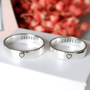 May include: Two silver rings with a heart engraved on each. The rings are on a white box with the number 250963 engraved on each ring.
