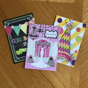 May include: Three greeting cards with different designs. The first card has a black background with a chalkboard design and the text "Congratulations to you". The second card has a pink background with a white wedding dress and the text "Here comes the bride". The third card has a yellow and white striped background with a purple and green party hat and the text "Celebrate".