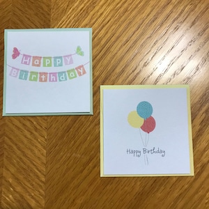 May include: Two birthday cards. The first card has a green border and features a banner with the text "Happy Birthday" and butterflies. The second card has a yellow border and features three balloons and the text "Happy Birthday".