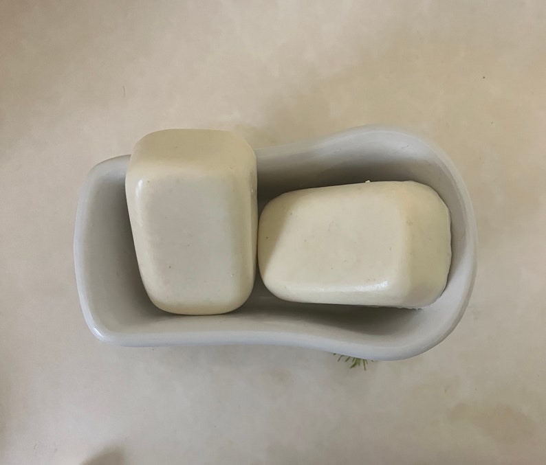 May include: Two white bars of soap in a white ceramic soap dish shaped like a bathtub.