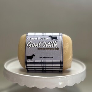 May include: A bar of goat milk soap with a white and black plaid label that reads "Pure Poshy - Goat Milk - Natural Colorants Soap" and "Net Weight 5.00 Oz".