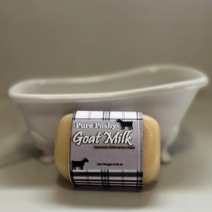 May include: A bar of goat milk soap with a black and white plaid label that reads "Pure Poshy - Goat Milk - Natural Colorants Soap - Net Weight 5.00 Oz."