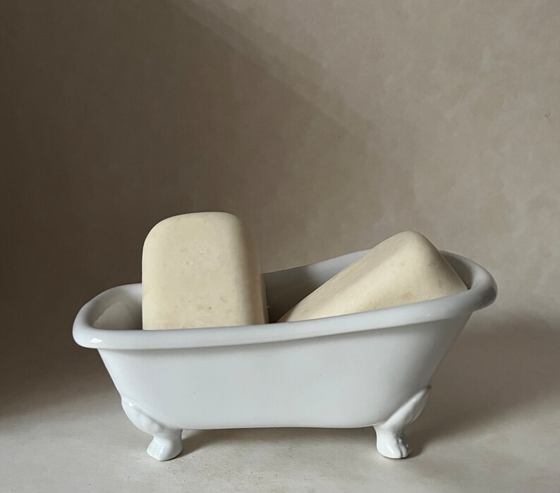 May include: Two white bars of soap in a white porcelain bathtub-shaped soap dish with three feet.
