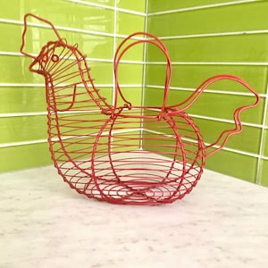 May include: A bright red wire basket shaped like a chicken, featuring a rounded body, a defined head with a comb, a curved tail, and a central handle. The structure is crafted from thin metal wire formed into a grid pattern for storage.