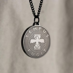 May include: A black chain necklace with a round silver pendant. The pendant features an eagle with outstretched wings, a sundial, and the words "TEMPUS FUGIT" around the edge.